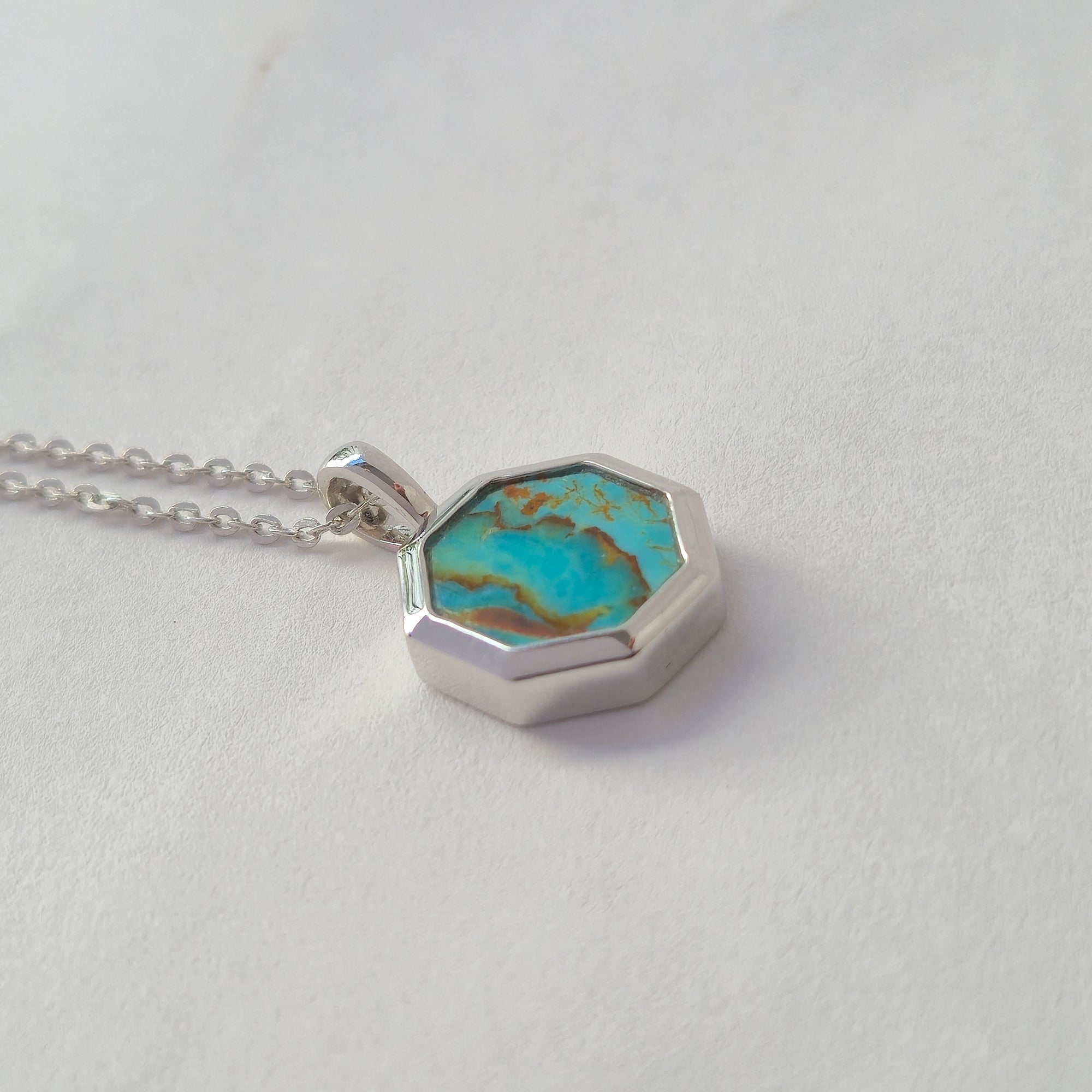 Turquoise stone pendant on a silver chain against a light gray background