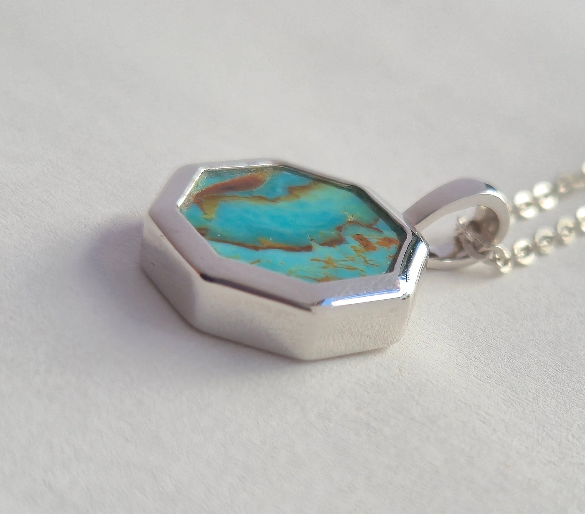 Necklace with a hexagonal pendant featuring turquoise stone on a light gray background