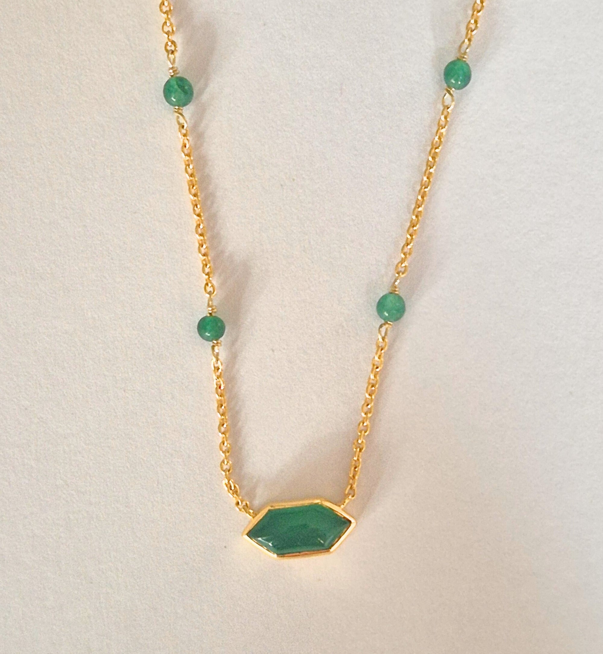 Gold necklace with green gemstones on a light gray background