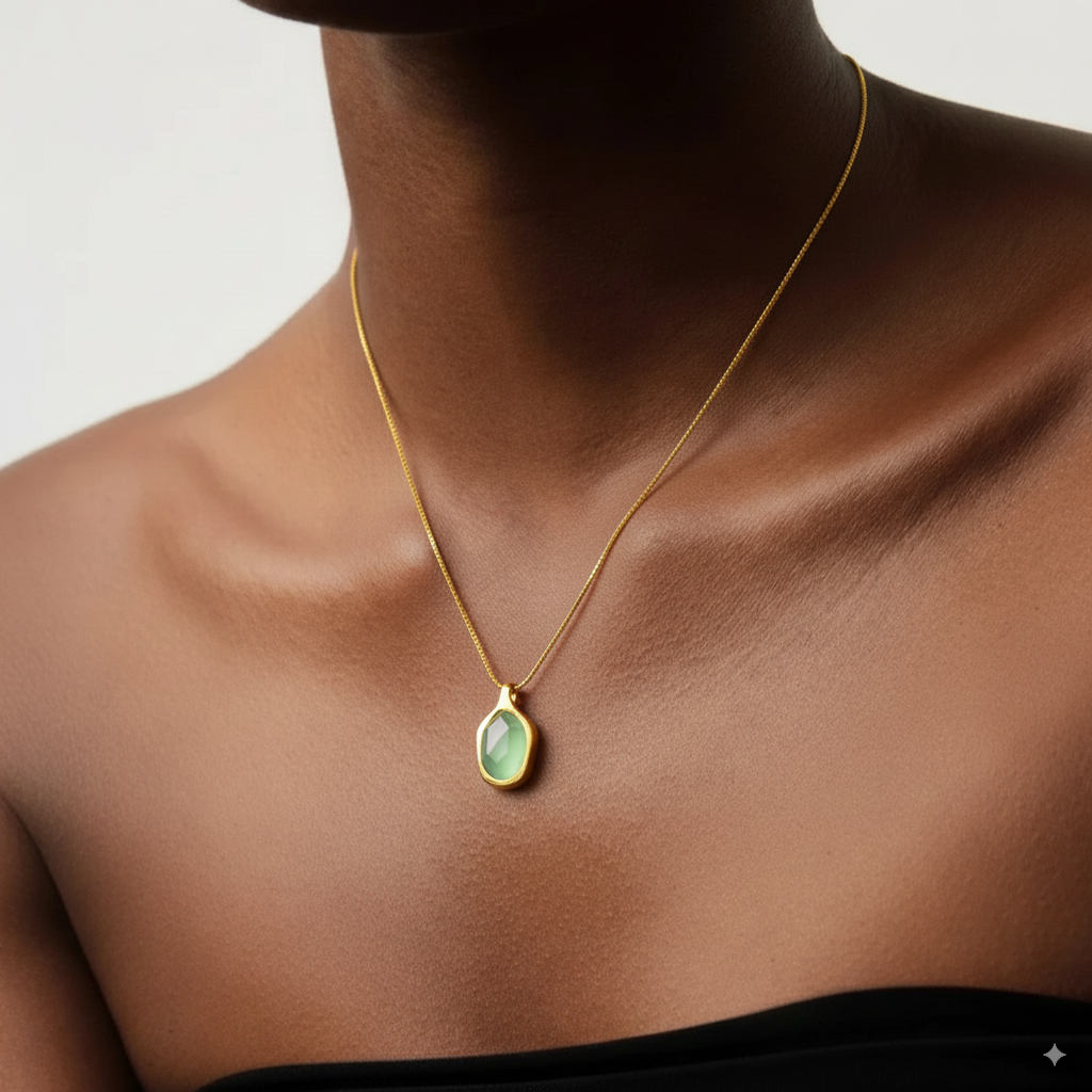 Gold necklace with a pendant on a person wearing a dark top against a neutral background